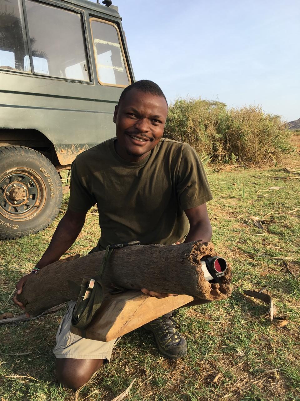 Wickliffe Odera holding a finished pole camera rig, a camera housed inside a section of tree trunk
