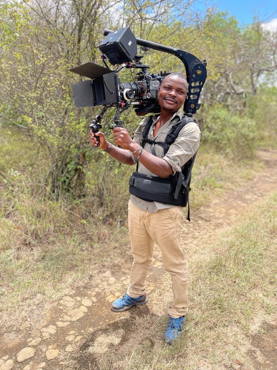 Wickliffe Odera carrying a DJI Ronin gimbal on an Easyrig while filming in the bush
