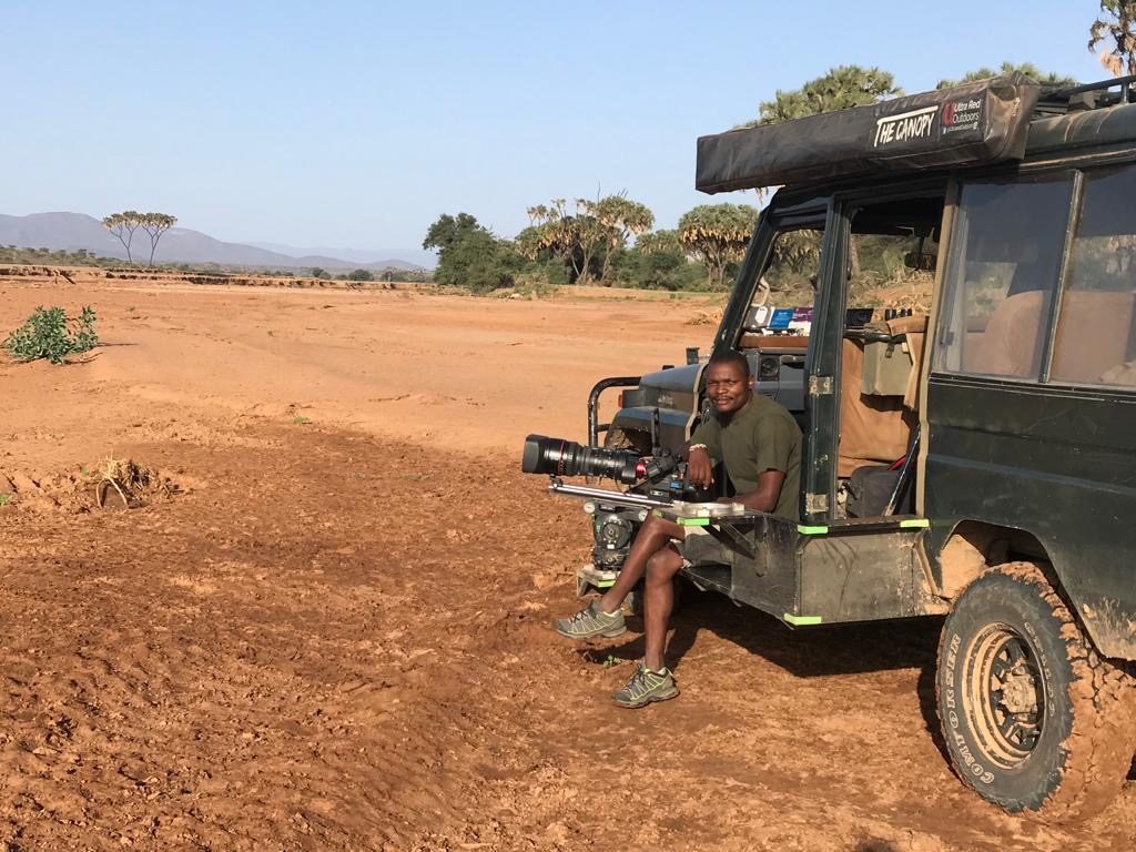Wildlife camera car with long lens tracking vehicle on open red-earth plains, Kenya